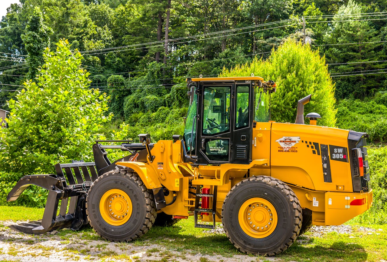 Yellow wheel loader parked outdoors in a forested area, showcasing machinery and natural contrast.